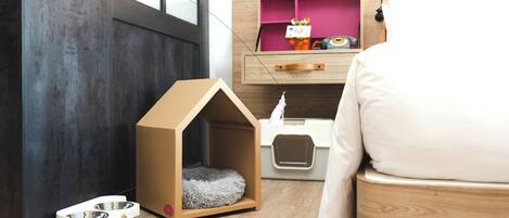A pet-friendly room with a wooden bed, a pet house, a litter box, and a pet bowl.