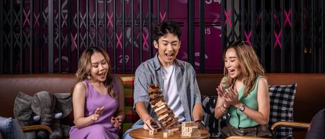A group of people playing a game of Jenga on a small table in a cozy indoor setting with a patterned wall in the background.