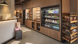 A modern hotel lobby with a reception desk, a refrigerated beverage display, and snack shelves. - Moxy Paris Clamart (Clamart)