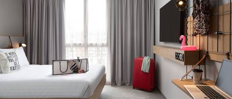 Una habitación de hotel moderna con una cama, un escritorio con una computadora portátil, una maleta y una ventana con cortinas.