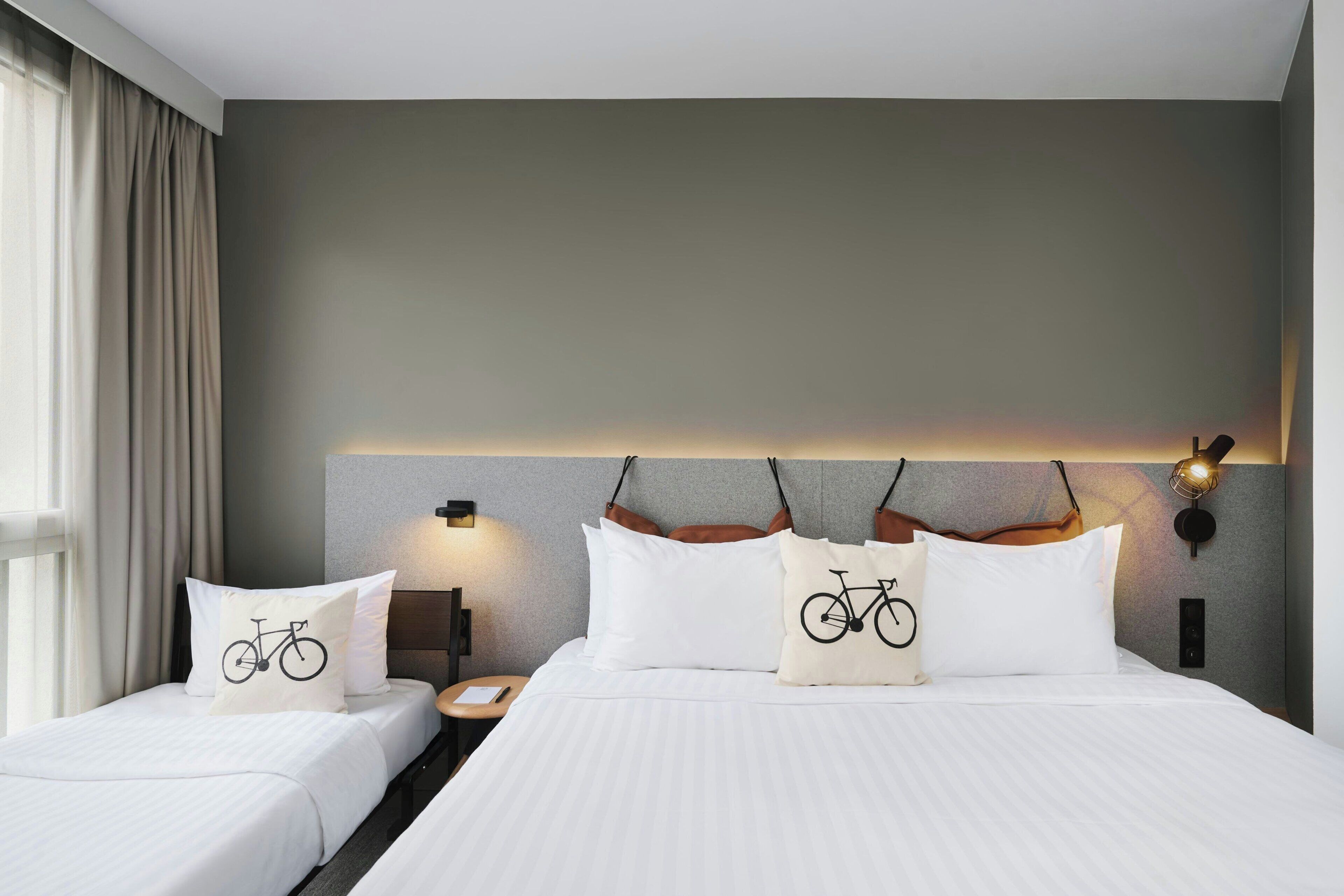 A hotel room with a large bed, two bedside tables, a nightstand, and a wall-mounted lamp.