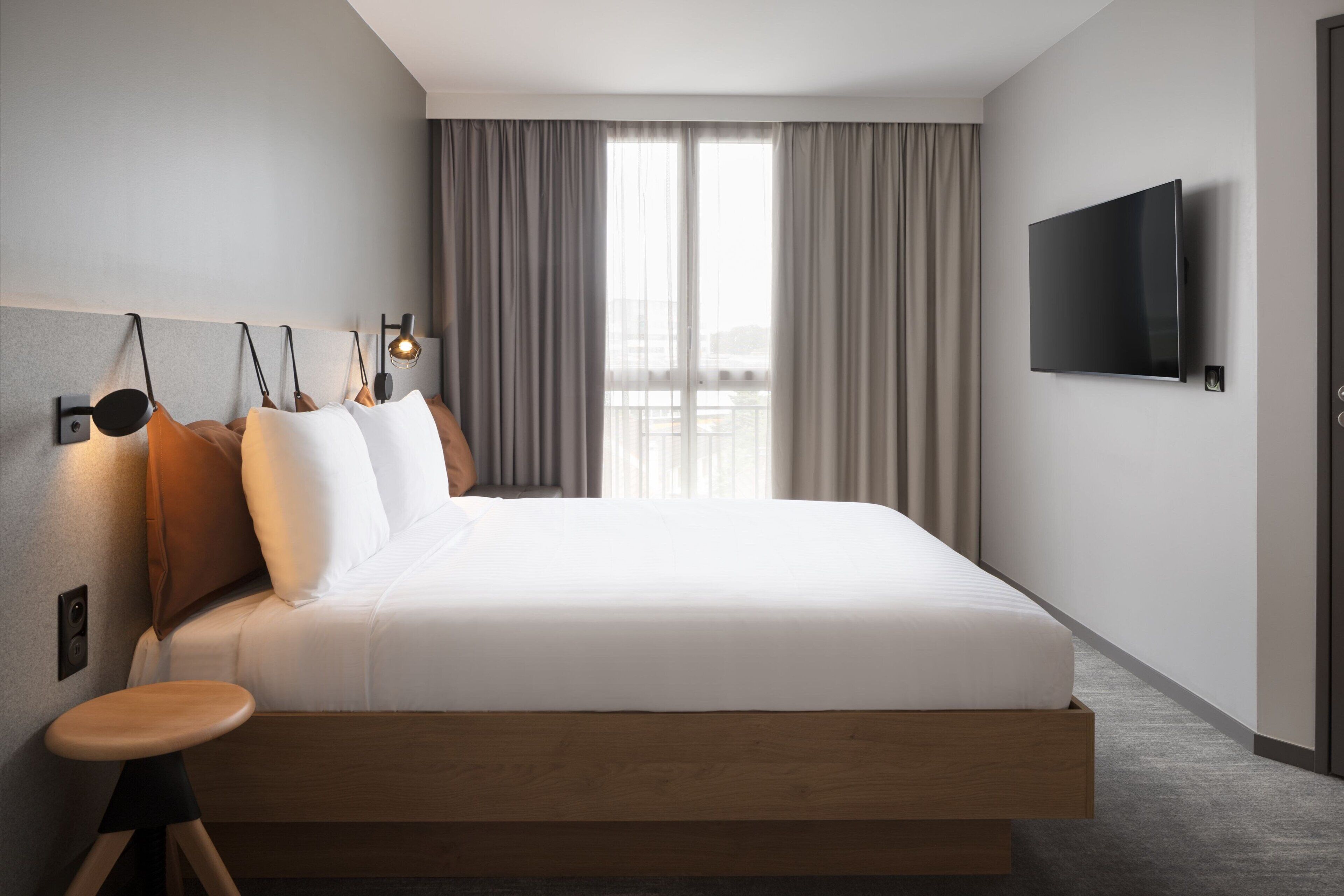 Een moderne hotelkamer met een groot bed, een aan de muur bevestigde televisie en uitzicht op de stad door het raam.