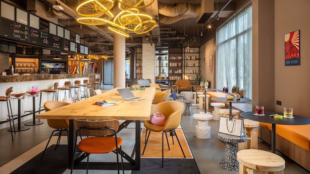 A modern library with a long wooden table, comfortable seating, and bookshelves. - Moxy Paris Clamart (Clamart)