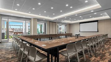 A conference room with a long table, chairs, a projector screen, and large windows.