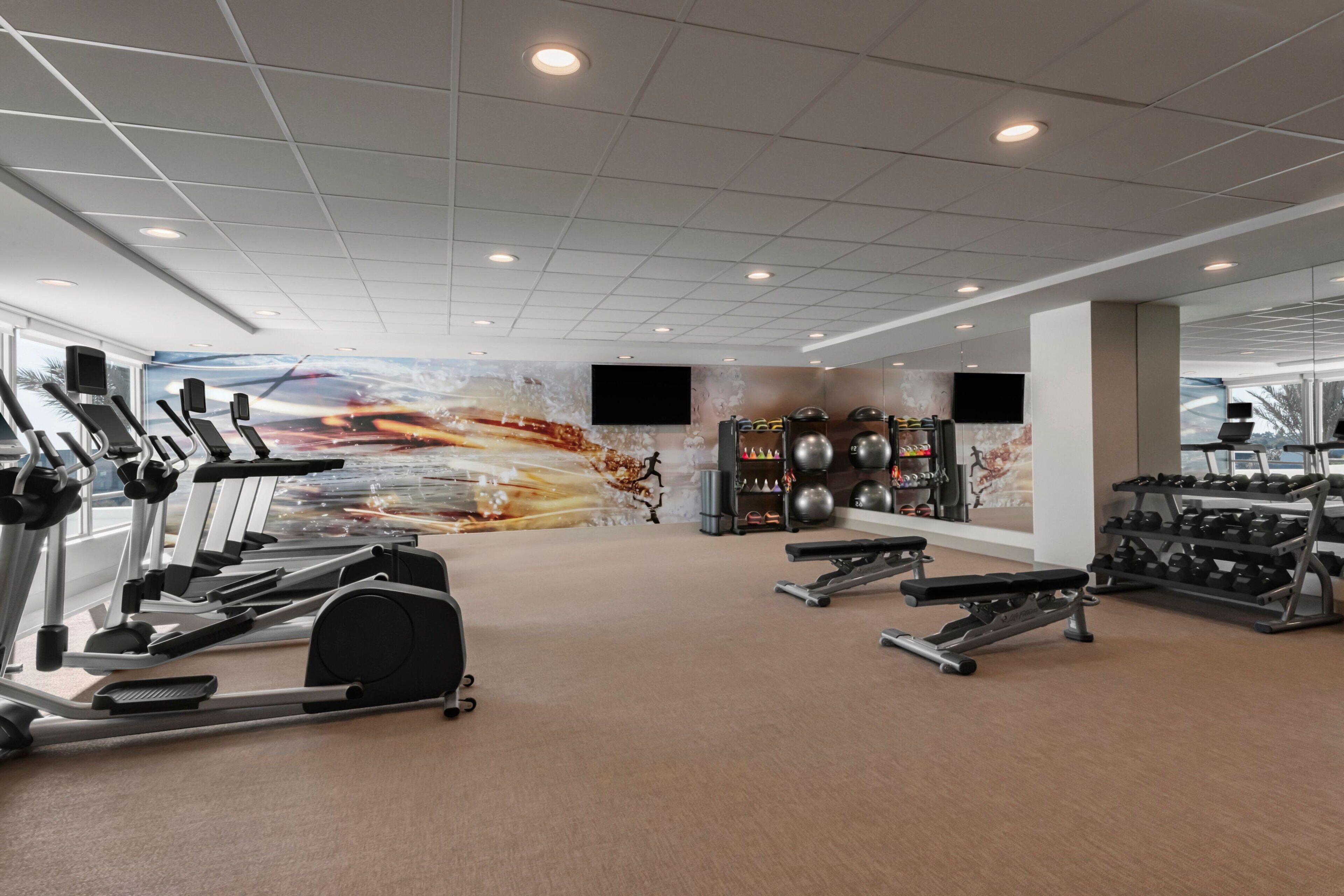 Un gimnasio moderno con máquinas de cardio, estaciones de pesas y un gran mural en la pared.