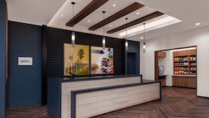 A modern reception area with a wooden reception desk, a large artwork above it, and a snack bar in the background. - SpringHill Suites by Marriott Chula Vista Eastlake (Chula Vista)
