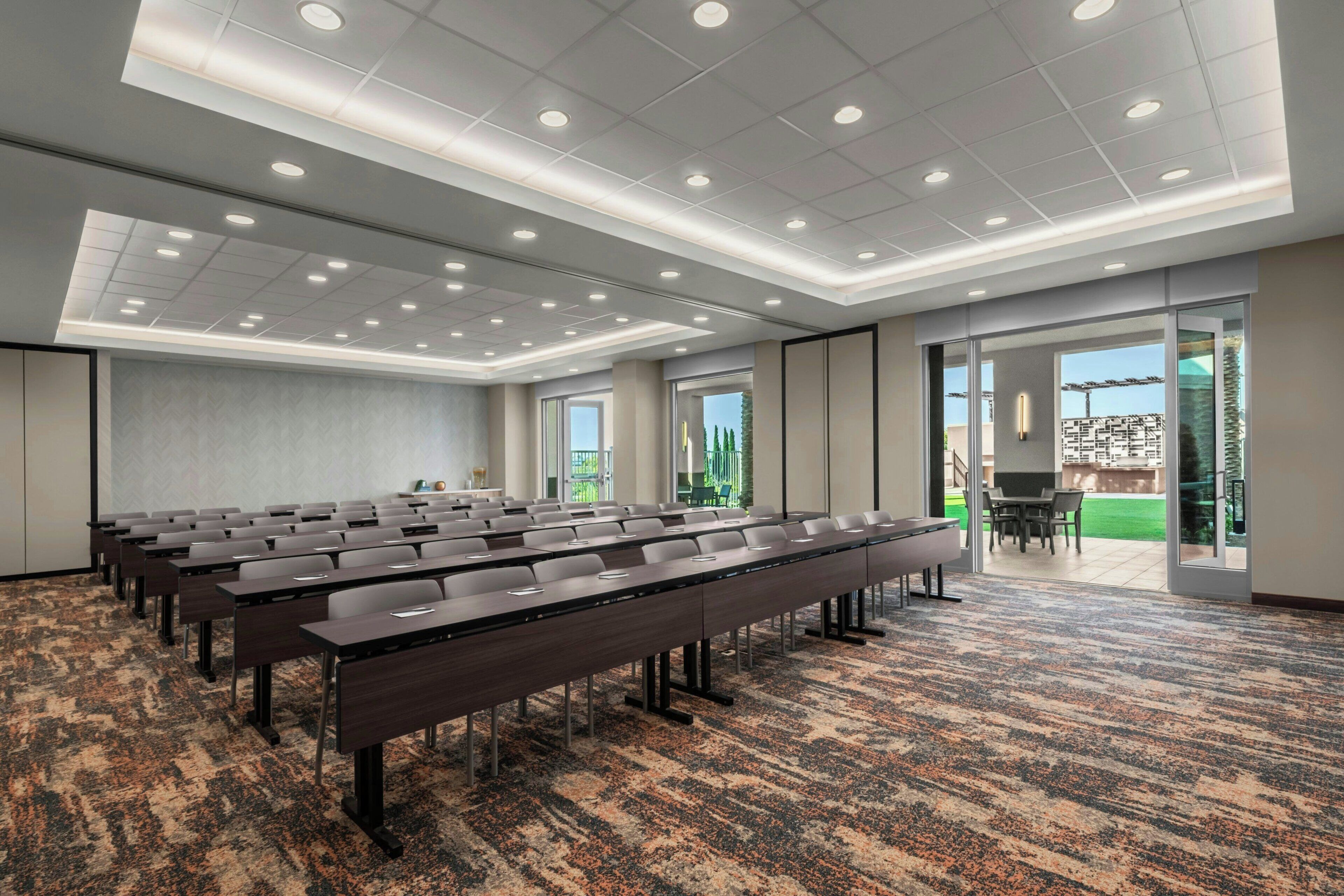 A conference room with rows of tables and chairs, large windows, and a carpeted floor.