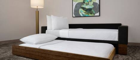 A neatly made bed with a wooden frame and white bedding, a floor lamp, and a framed abstract painting on the wall.