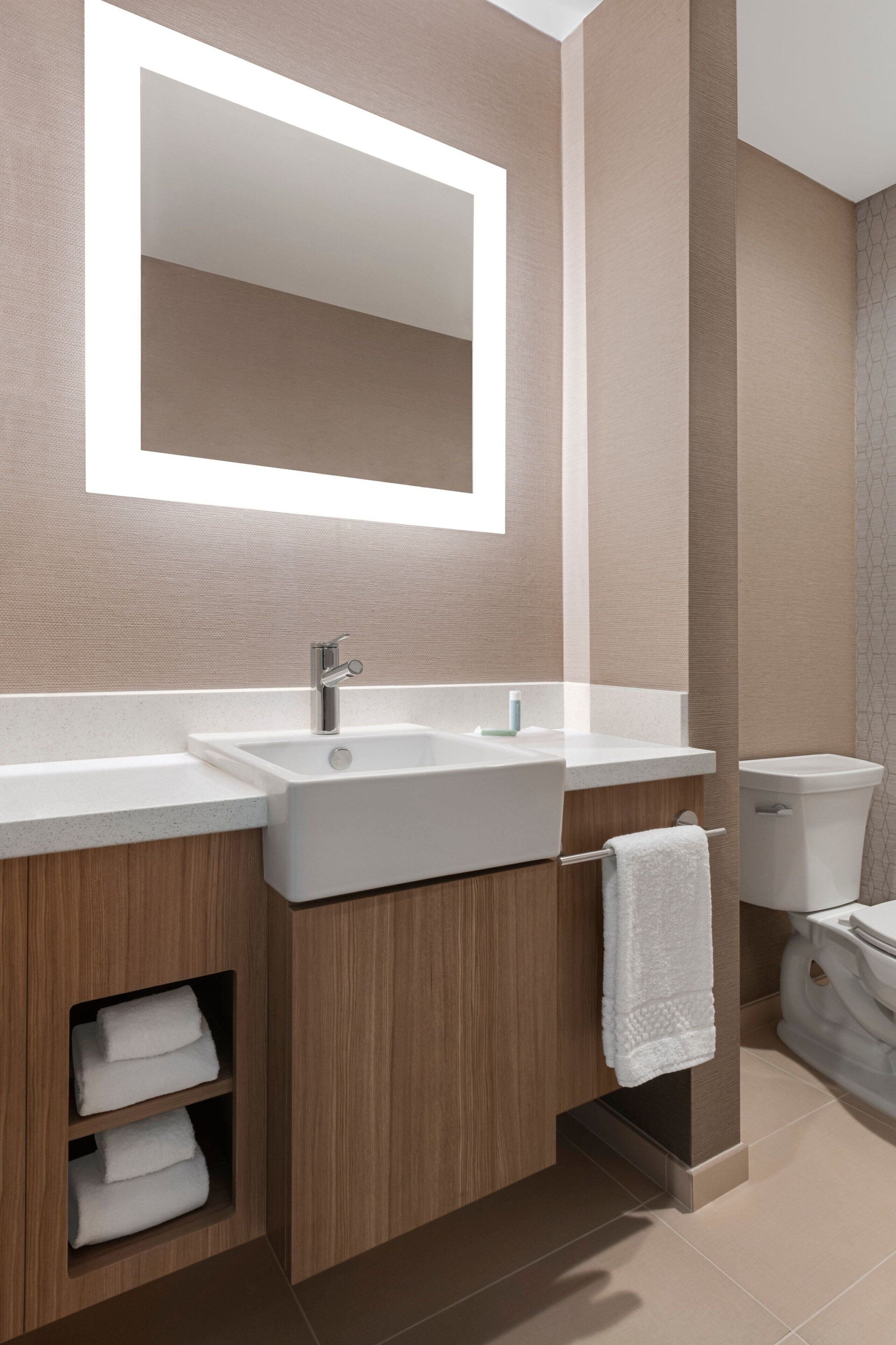 A modern bathroom with a large mirror, a sink, and a toilet.