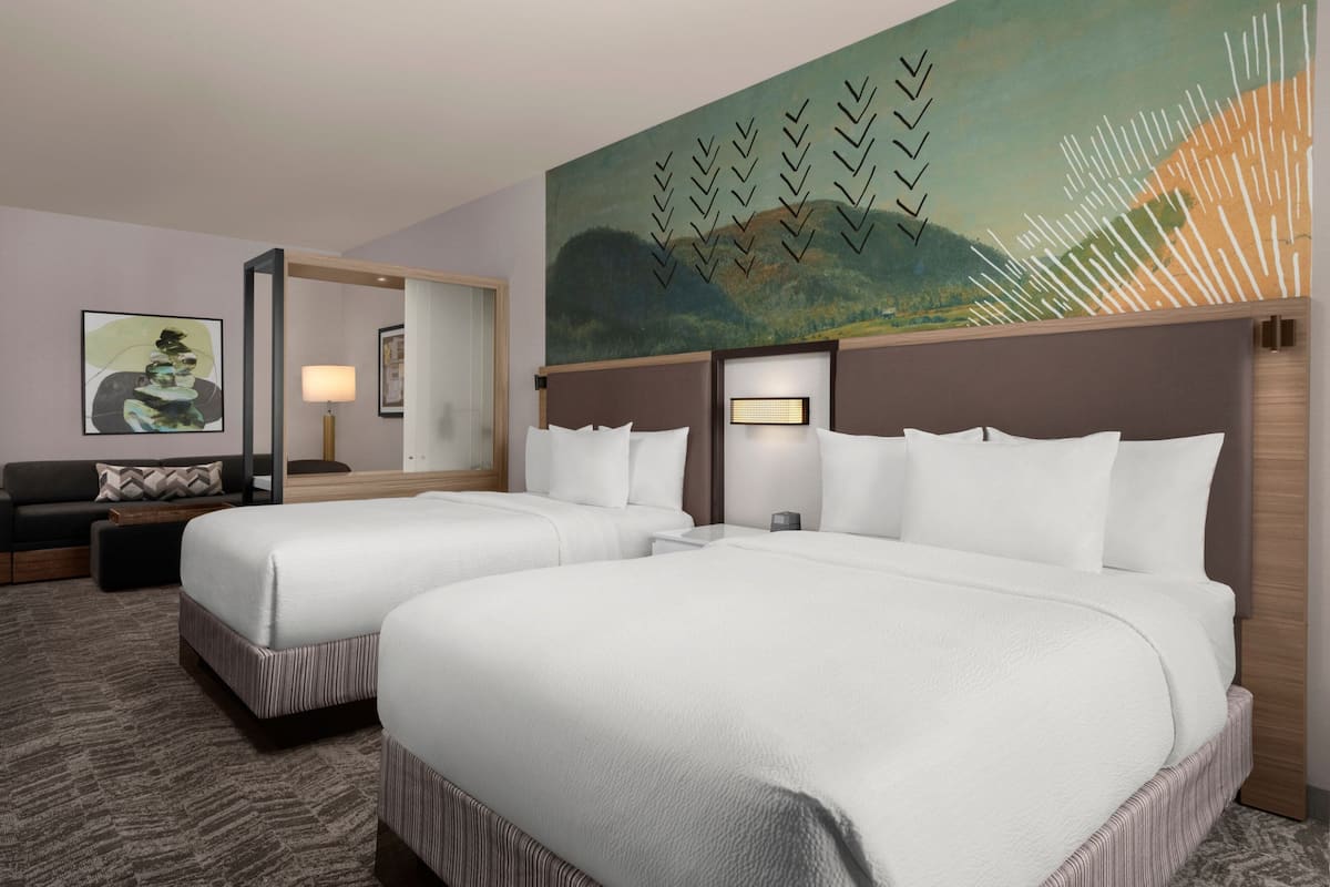 A hotel room with two beds, a sofa, a painting, and a lamp.