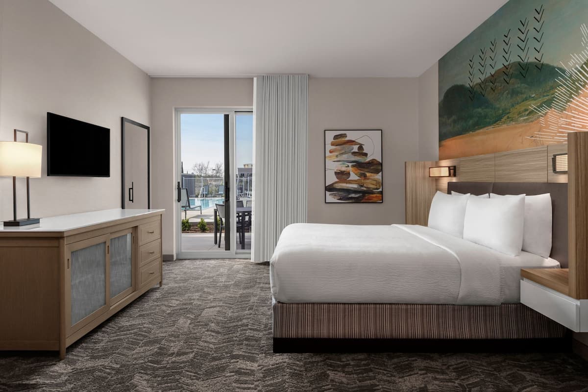 A hotel room with a bed, a TV, a desk, and a painting.