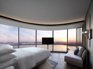 Ein modernes Hotelzimmer mit gewölbter Decke, einem großen Bett, einer Couch, einem Fernseher und Blick auf einen Stadt-Horizont und Wasser.