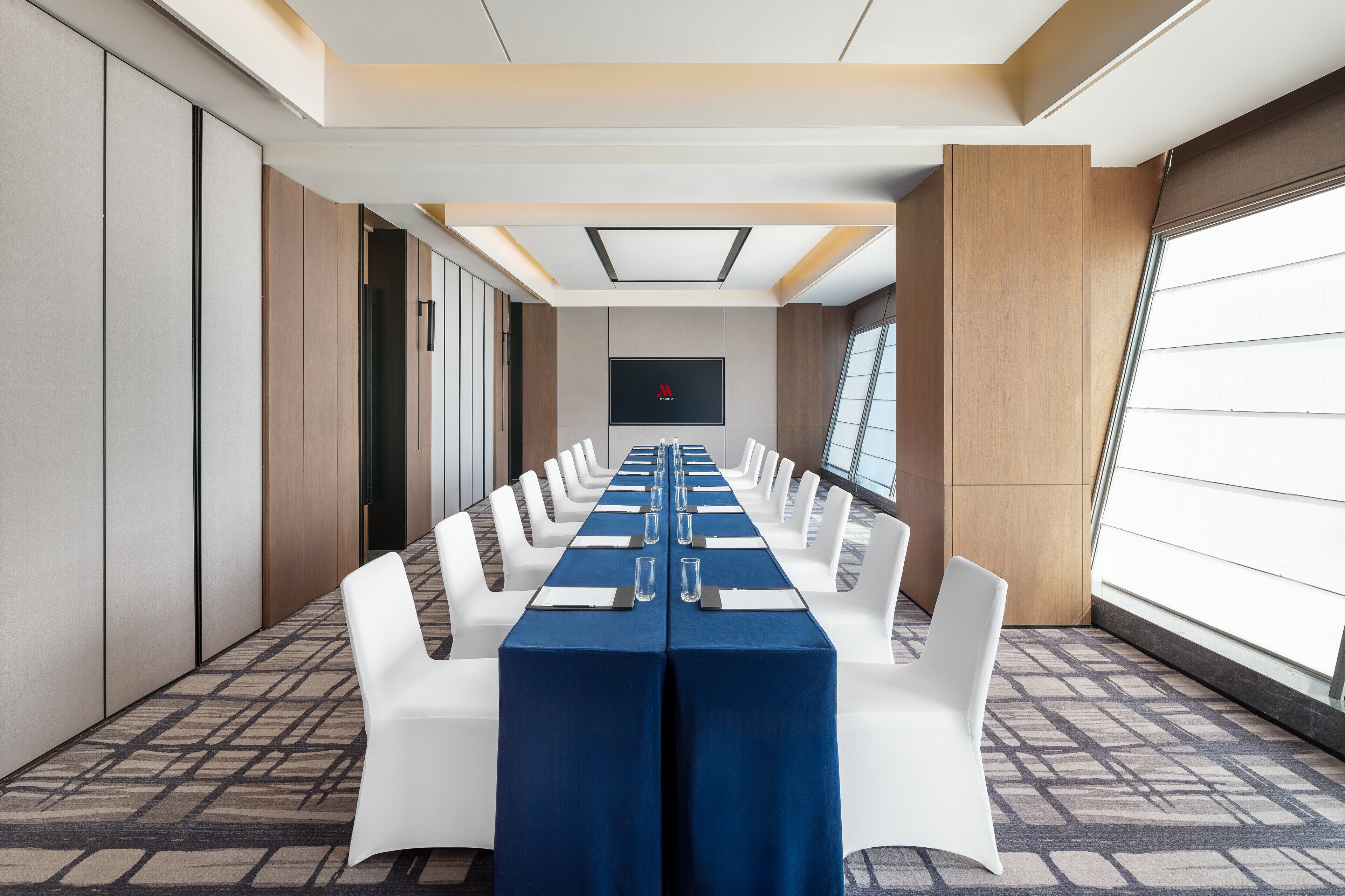 A conference room with a long table, white chairs, and a blue tablecloth.