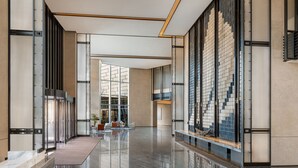 Un vestíbulo moderno con una recepción de mármol, puertas de cristal y una zona de estar con sillas y una mesita.