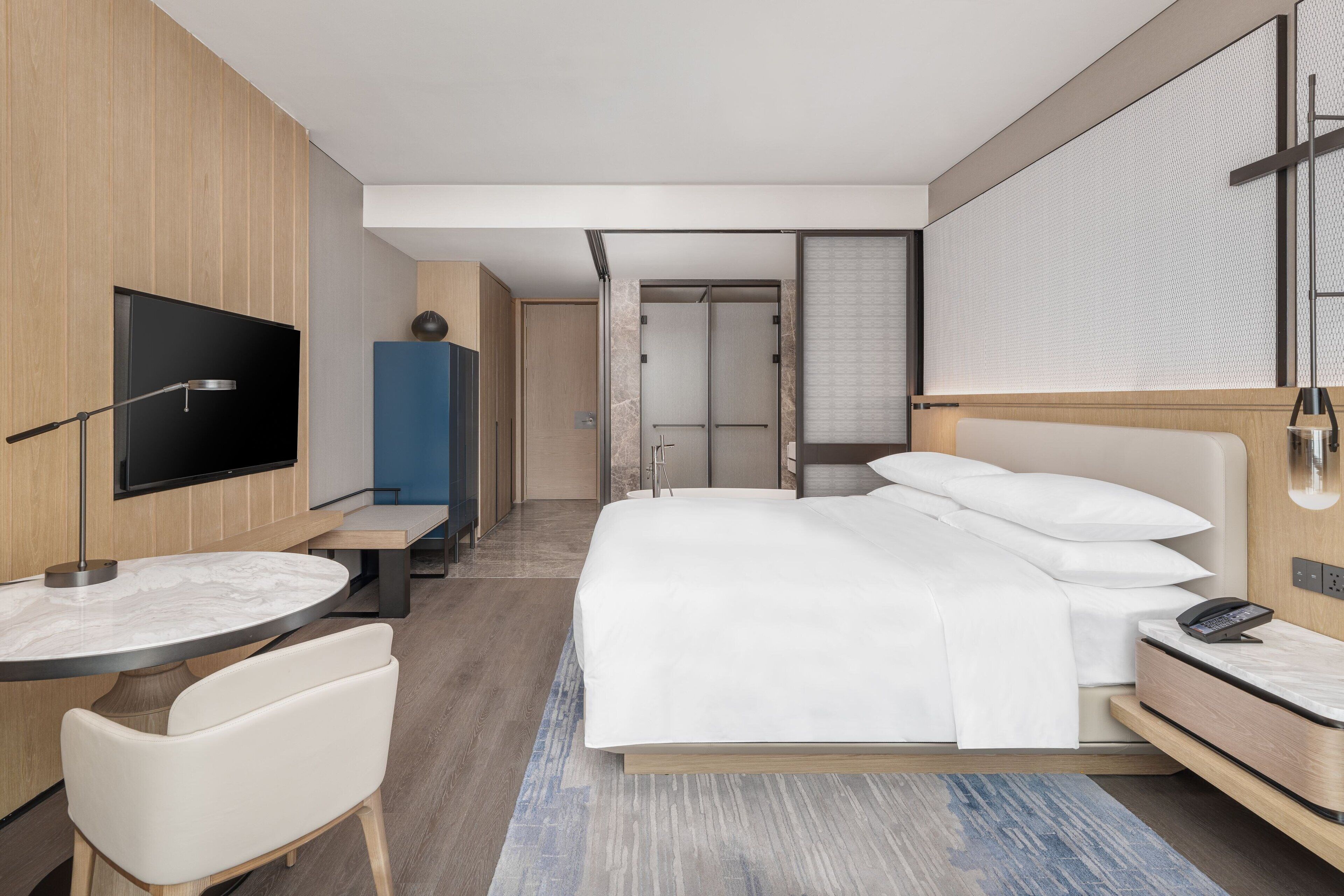 Una habitación de hotel moderna con una cama grande, un escritorio con una silla, un televisor y una zona de ducha.