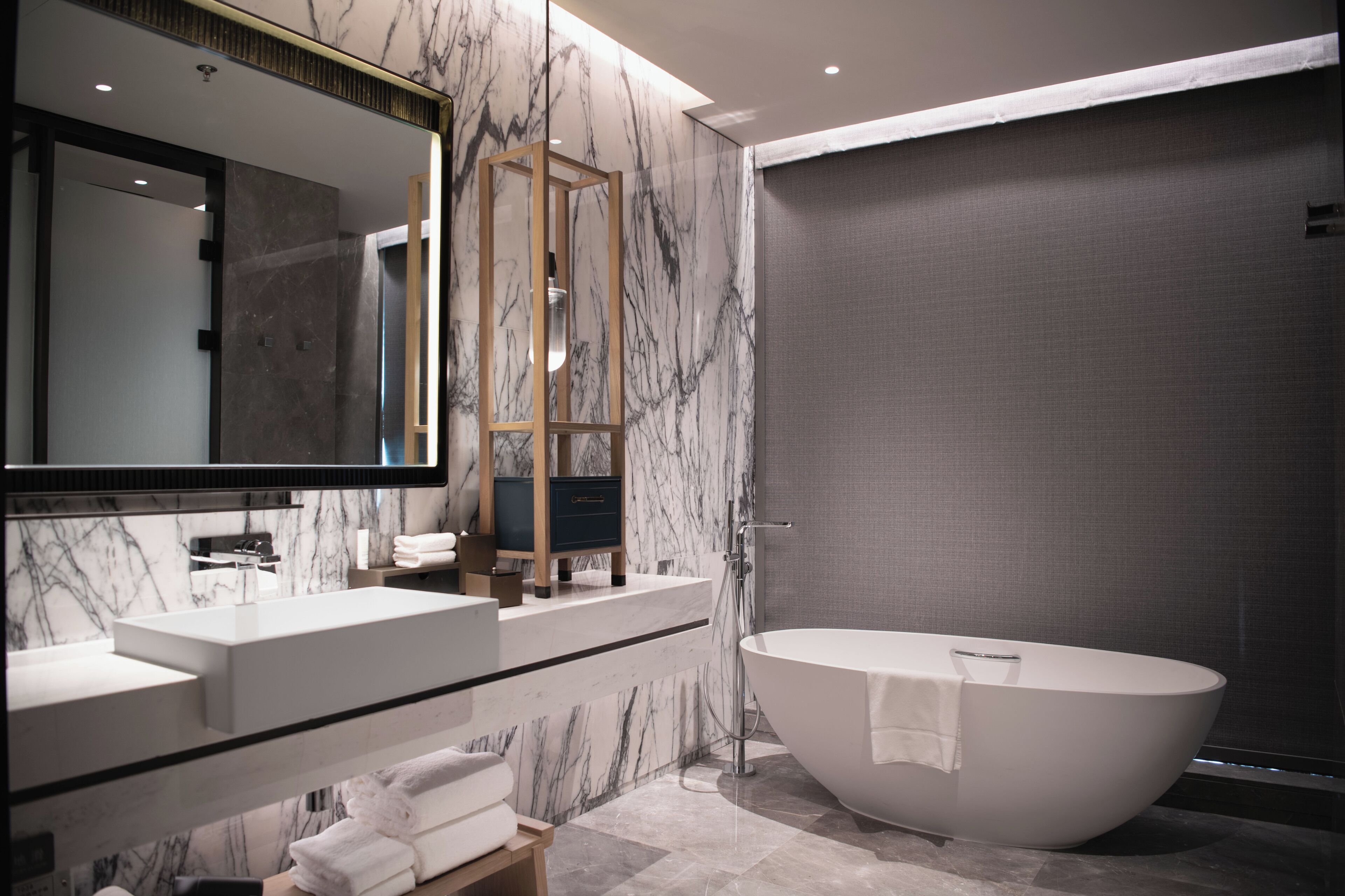 Ein modernes Badezimmer mit einer freistehenden Badewanne, einem großen Spiegel und Marmorwänden.