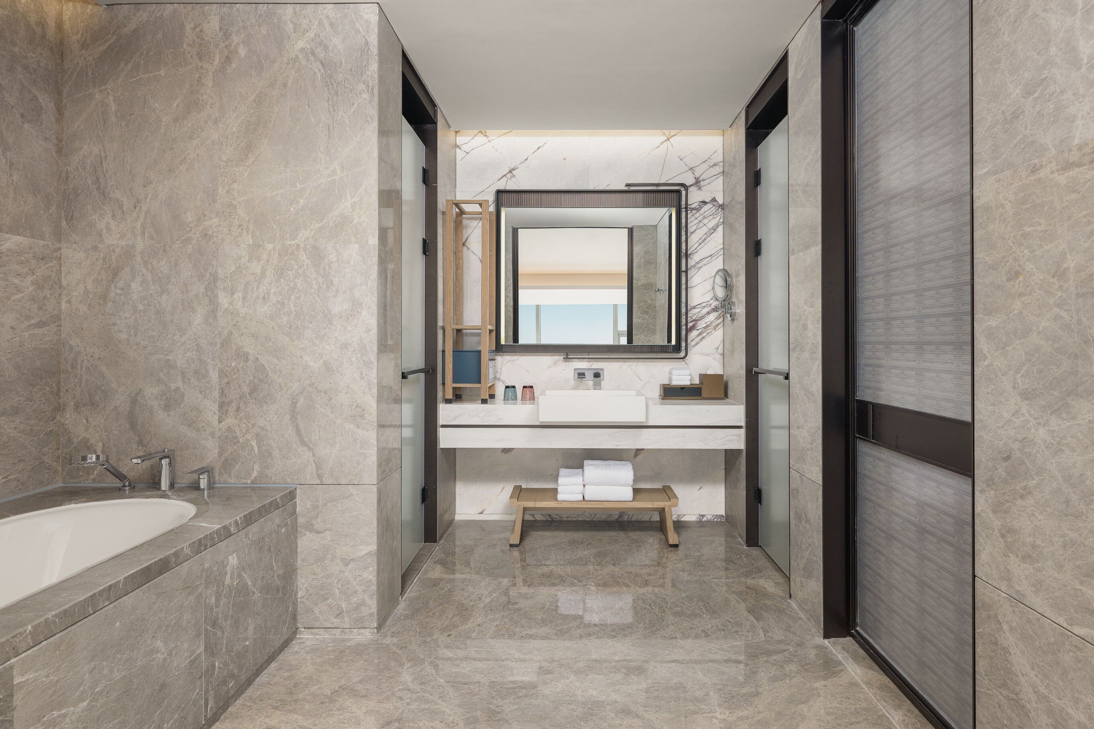 Un baño moderno con una bañera grande, un tocador con espejo y un banco.