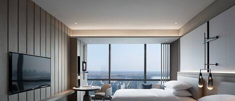 Habitación de hotel moderna con un televisor grande, una mesa redonda, dos camas y vista a la ciudad.