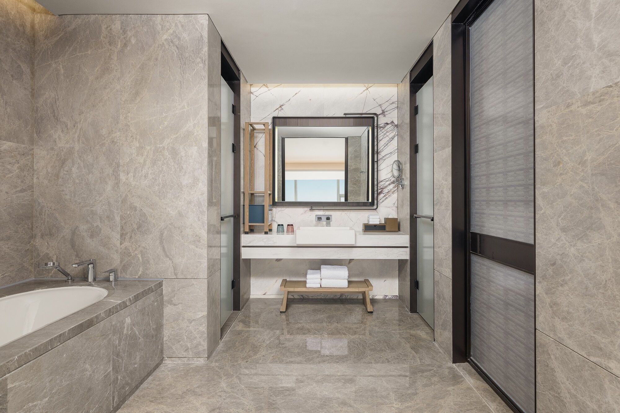 A modern bathroom with a bathtub, a sink with a mirror, and a bench.