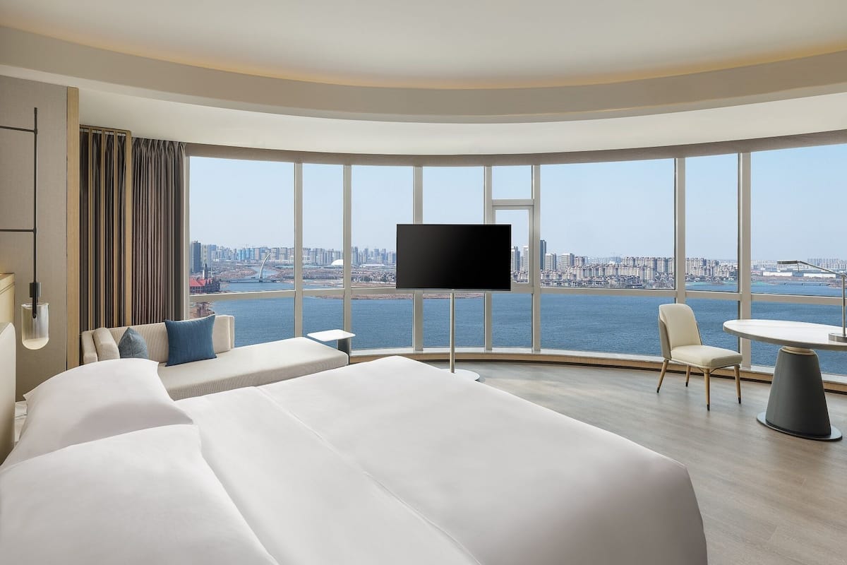 Habitación de hotel con una cama grande, televisión, zona de estar con mesa y vistas a la ciudad y al agua.