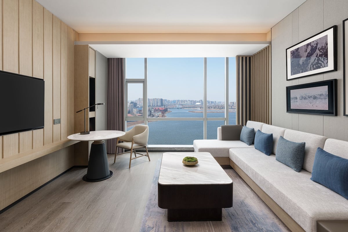 Una habitación de hotel moderna con un ventanal grande, un televisor de pantalla plana, una mesa redonda, un sofá y una mesa de centro.