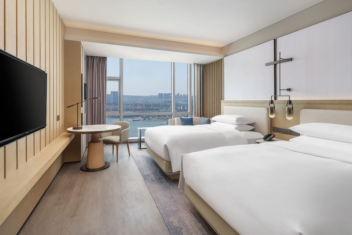Habitación de hotel con dos camas, televisión, una mesita y vista a la ciudad.