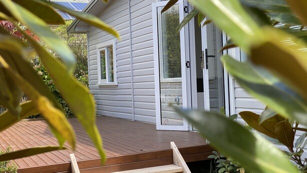 Una terraza de madera que conduce a una casa blanca con puerta corrediza de vidrio.