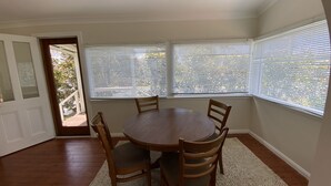 Comedor con mesa redonda y cuatro sillas de madera, ventanas amplias con persianas y una puerta que da al exterior.