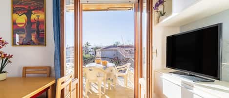 A balcony with a table and chairs, a TV on a white cabinet, and a painting on the wall.