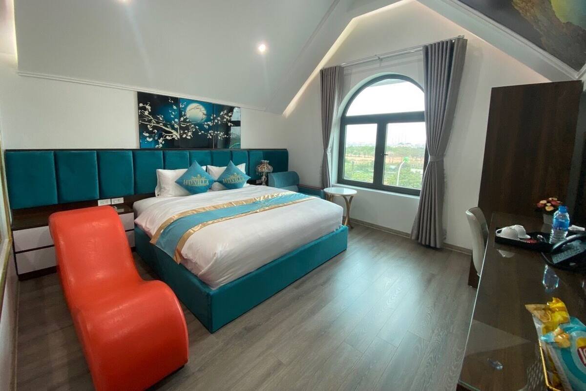 Une chambre à coucher moderne avec un grand lit, un banc rouge, un bureau et une fenêtre avec des rideaux.