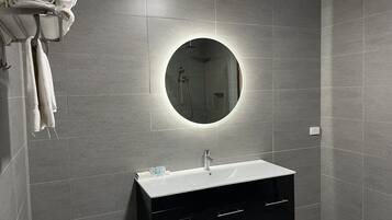 A modern bathroom with grey tiles, a round mirror, a black vanity with drawers, and a towel rack with folded towels.