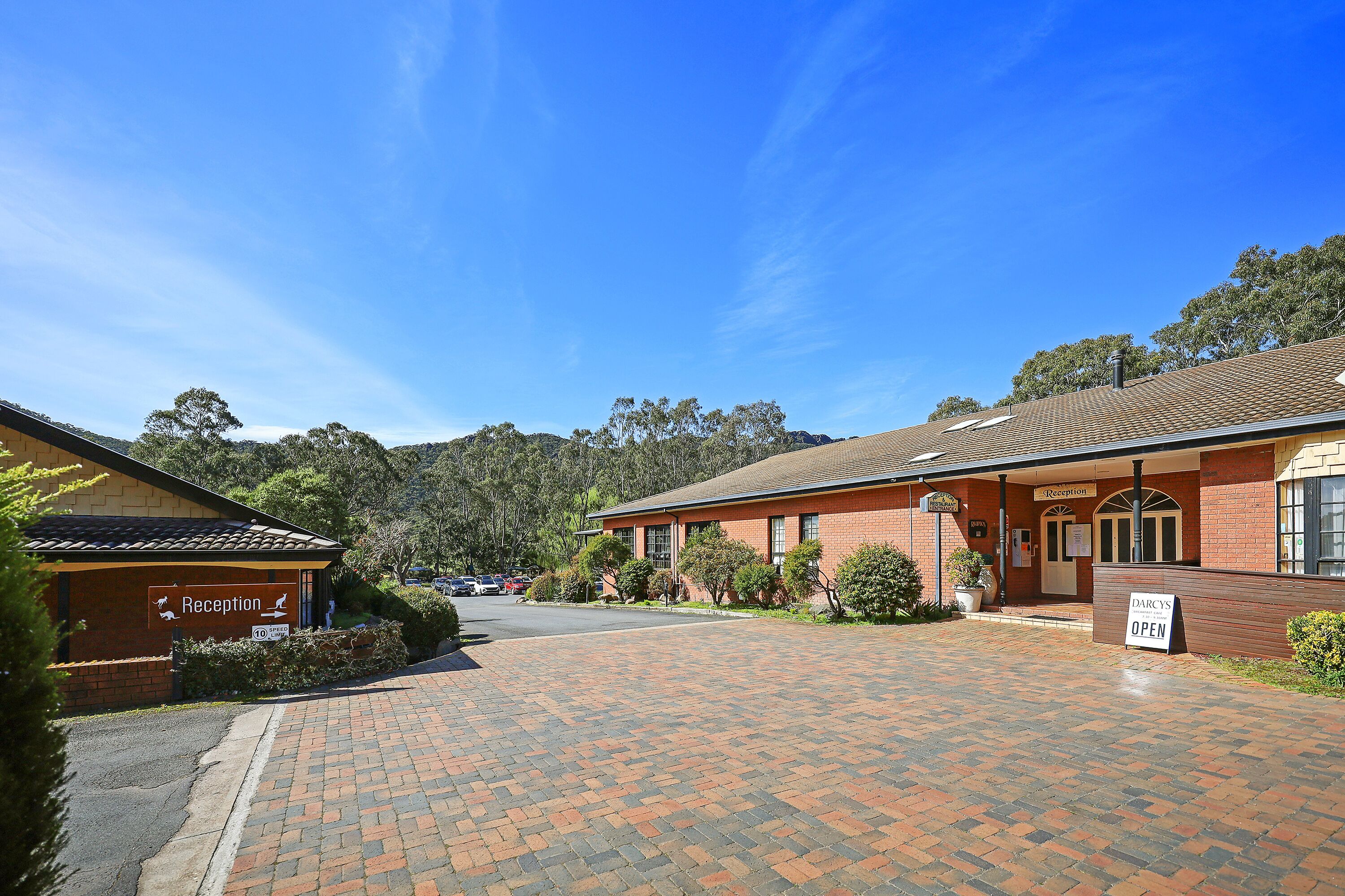 A reception area with a sign indicating it's open, a brick building, and a paved driveway leading to the entrance.