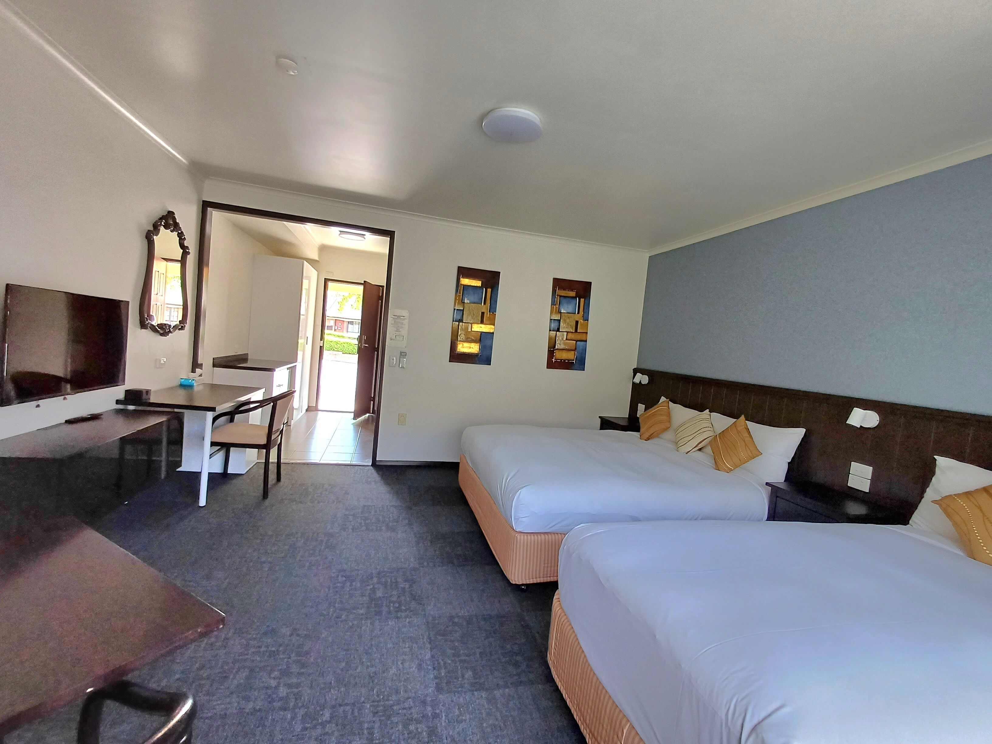 A hotel room with two beds, a desk, a chair, a TV, and a door leading outside.