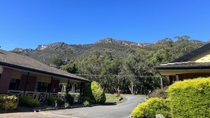 A building with a tiled roof and a covered porch, surrounded by greenery and a mountain in the background. - COUNTRY PLAZA HALLS GAP (Halls Gap)