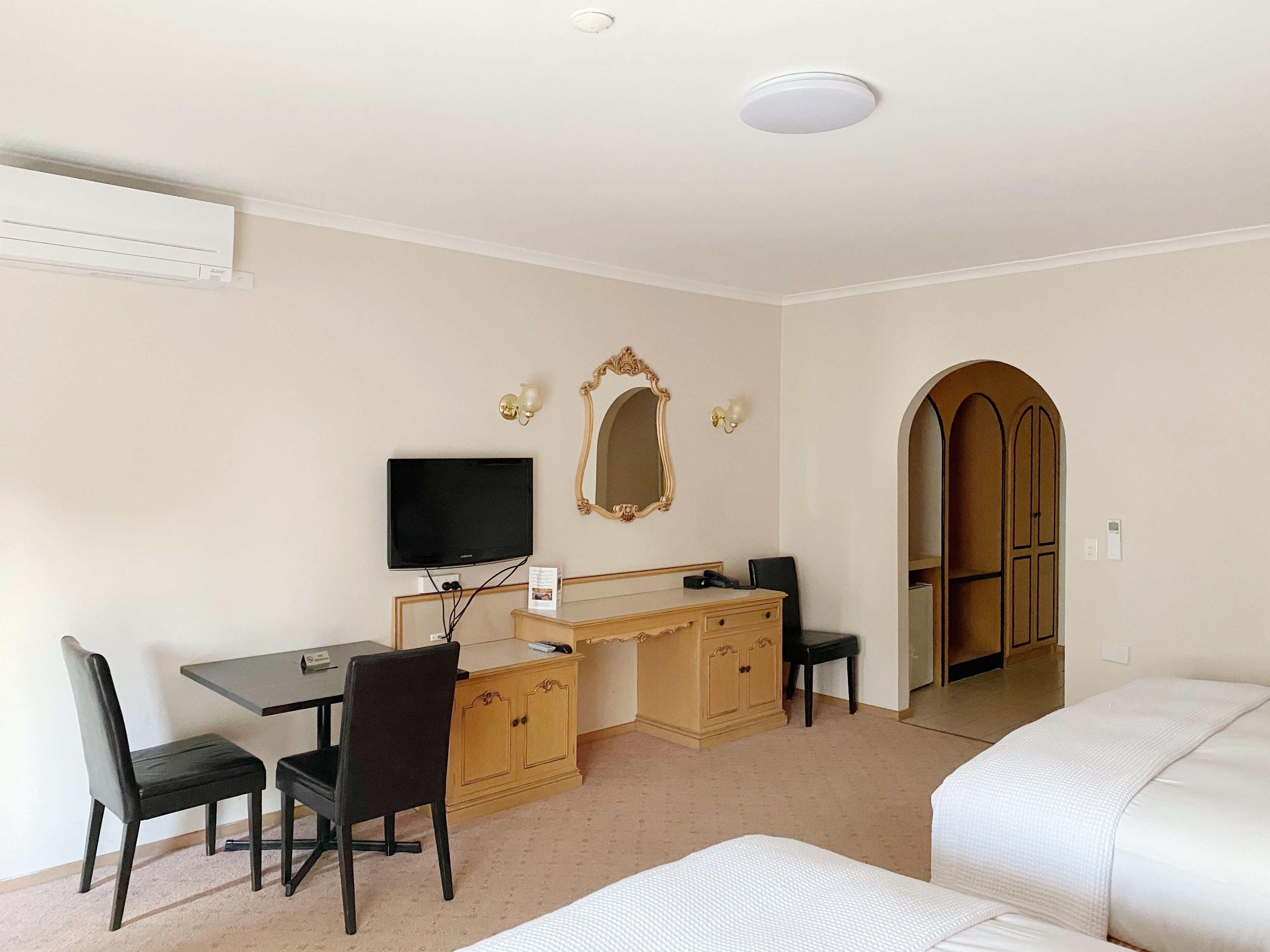 Une chambre d’hôtel équipée d’un bureau, de deux chaises, d’une télévision, d’un miroir et d’une armoire.