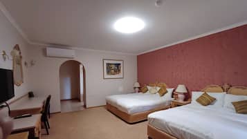 A hotel room with two beds, a desk, a chair, an air conditioning unit, and a painting on the wall.