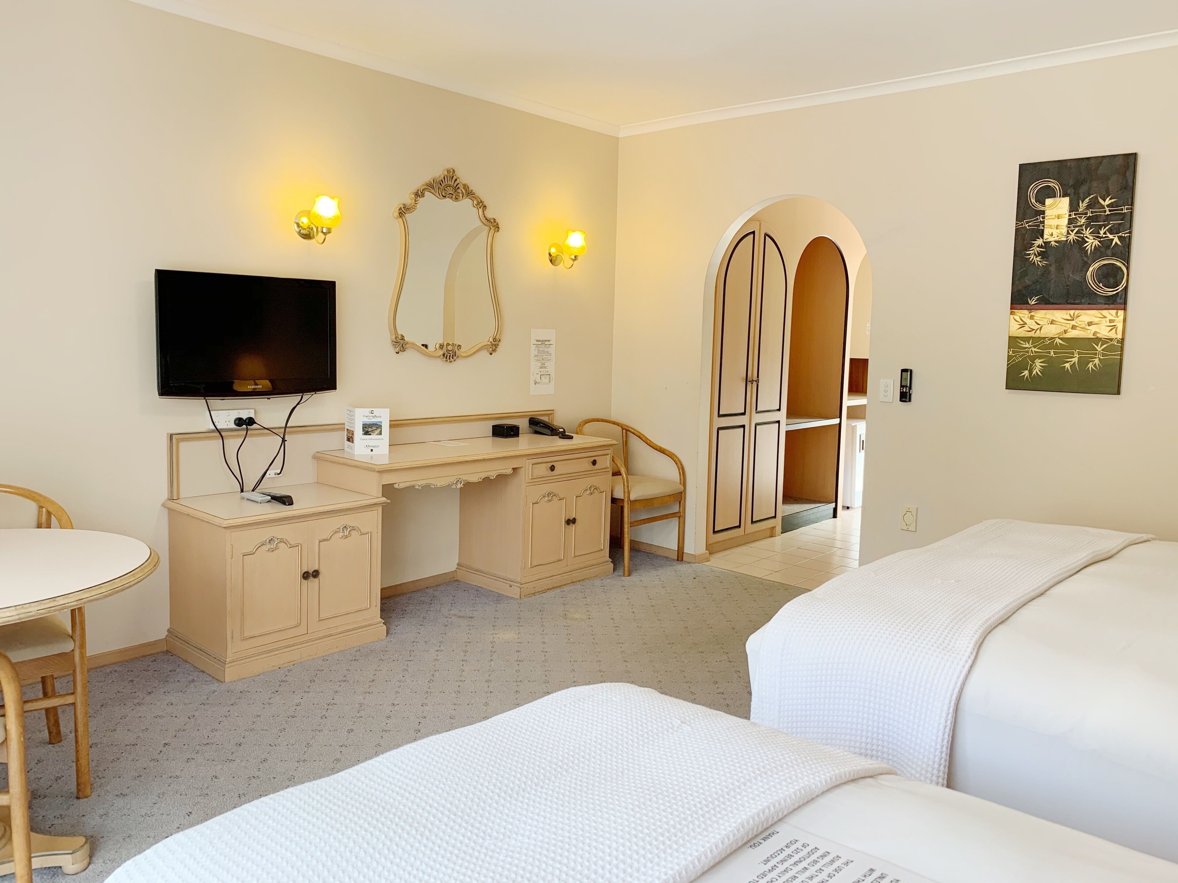 A hotel room with a bed, a desk, a chair, a television, a mirror, and a wardrobe.