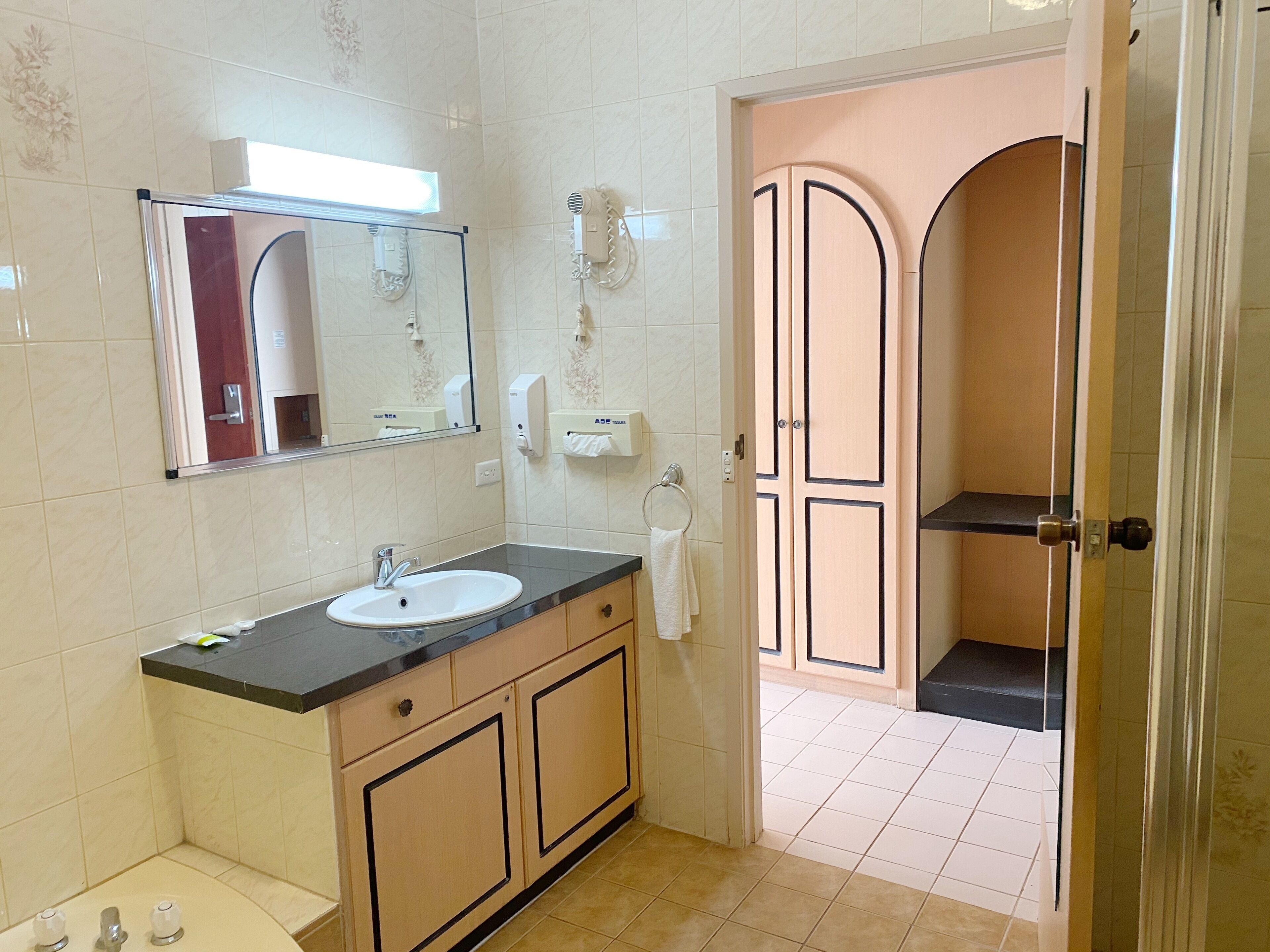 A bathroom with a sink, mirror, towel dispenser, and a shower area.