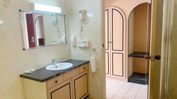 A bathroom with a sink, mirror, towel dispenser, and a shower area.