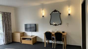 Habitación de hotel con cama, escritorio con dos sillas, televisor, espejo e iluminación en la pared.