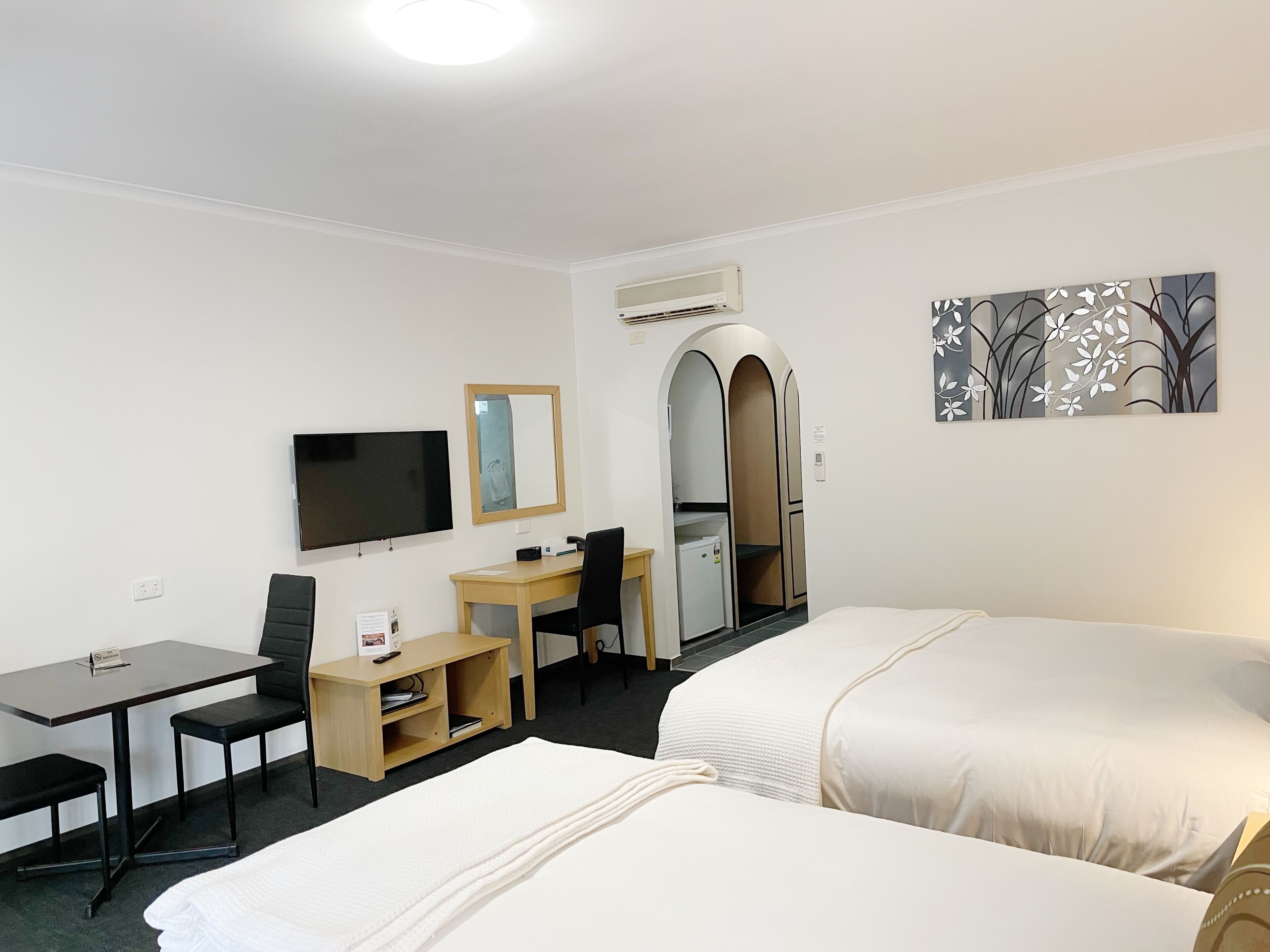 Une chambre d’hôtel avec deux lits, un bureau, une chaise, une télévision et une petite kitchenette.