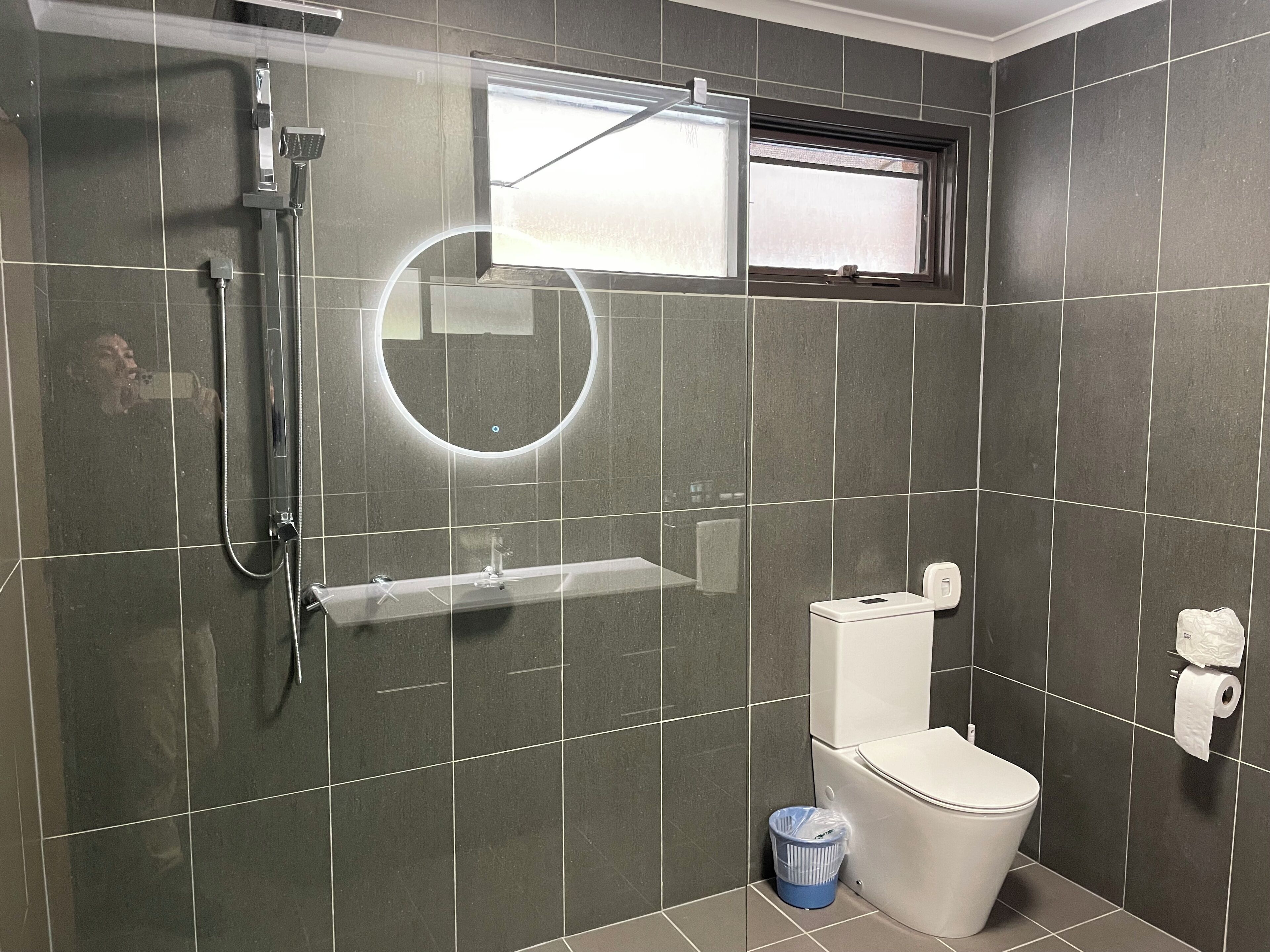 A bathroom with a shower, toilet, and a small window.