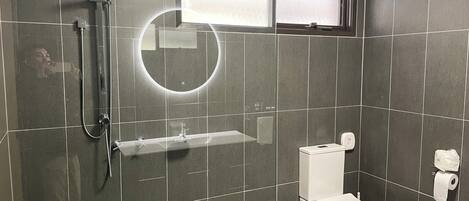 A bathroom with a shower, toilet, and a small window.