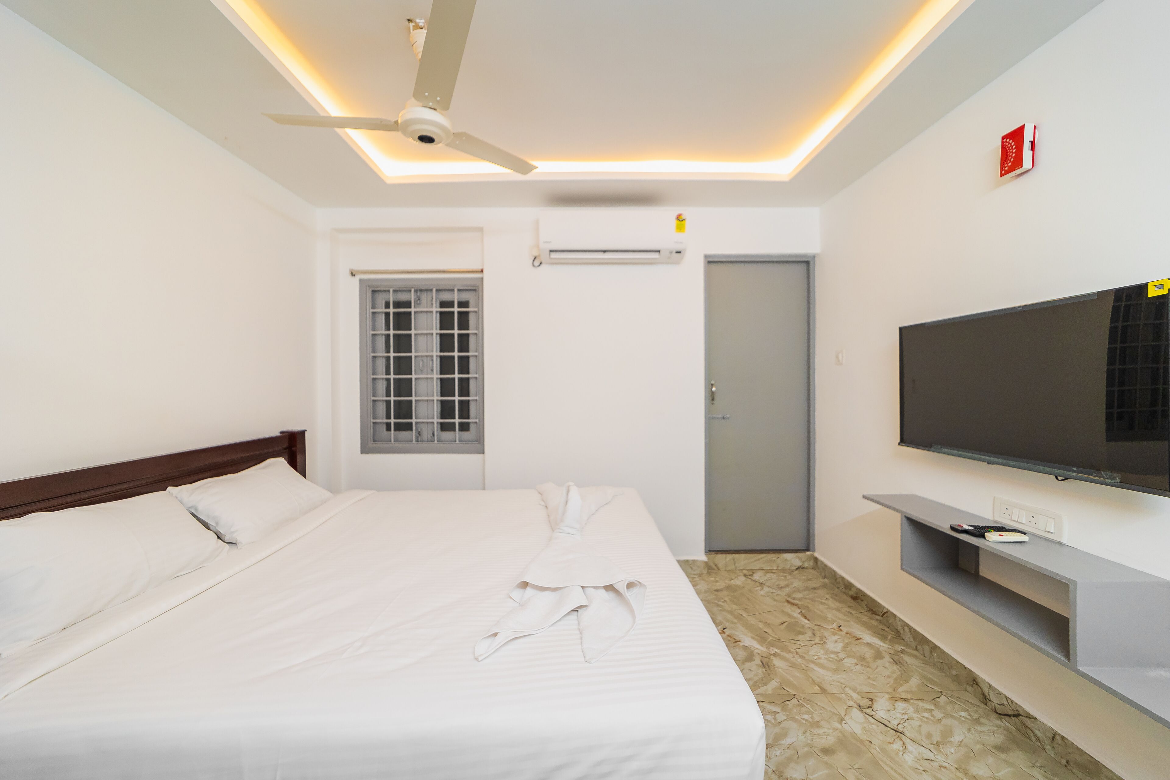 Una habitación de hotel con una cama, ventilador de techo, televisión y puerta.