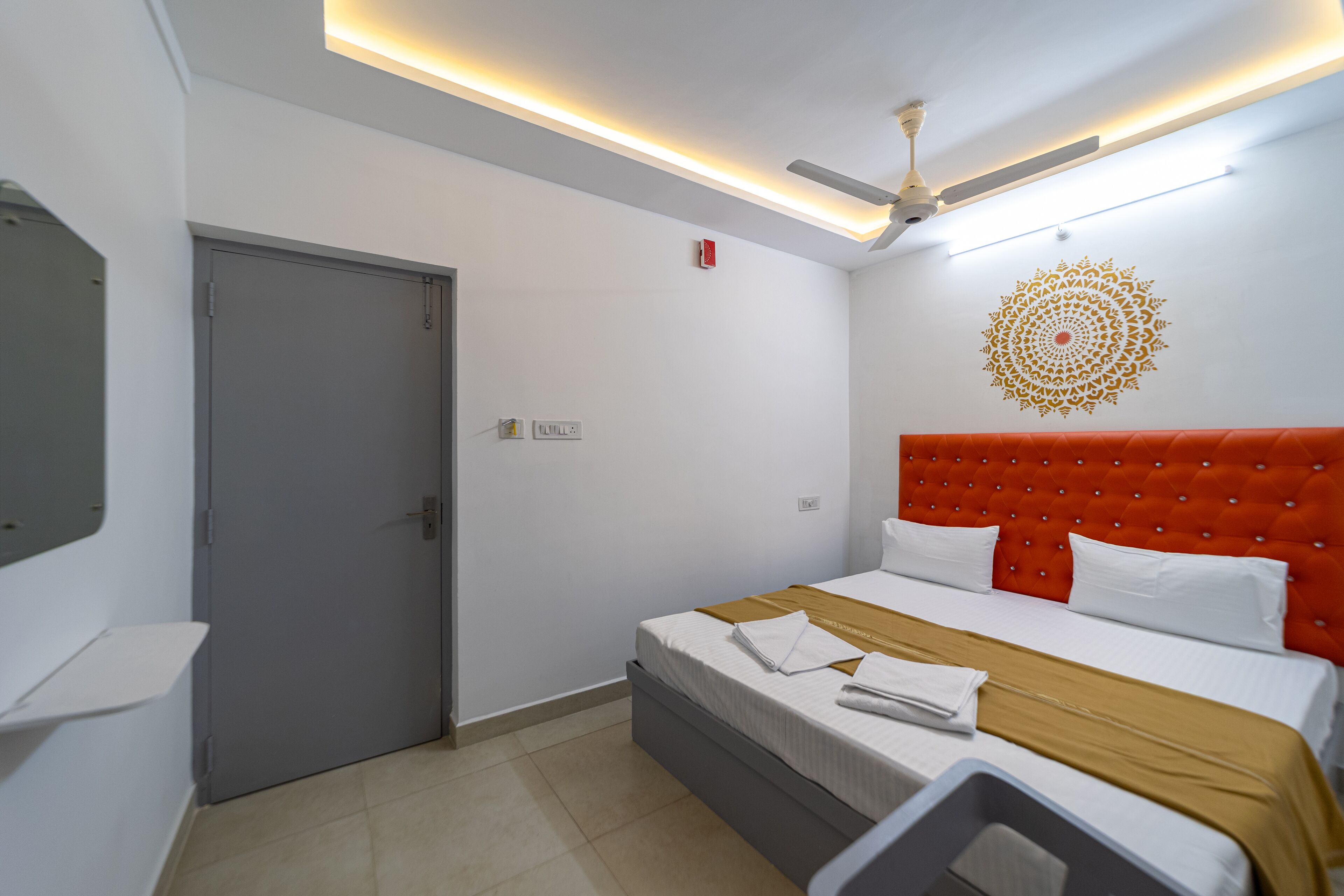 Quarto de hotel com cama, ventilador de teto, decoração na parede e uma porta.