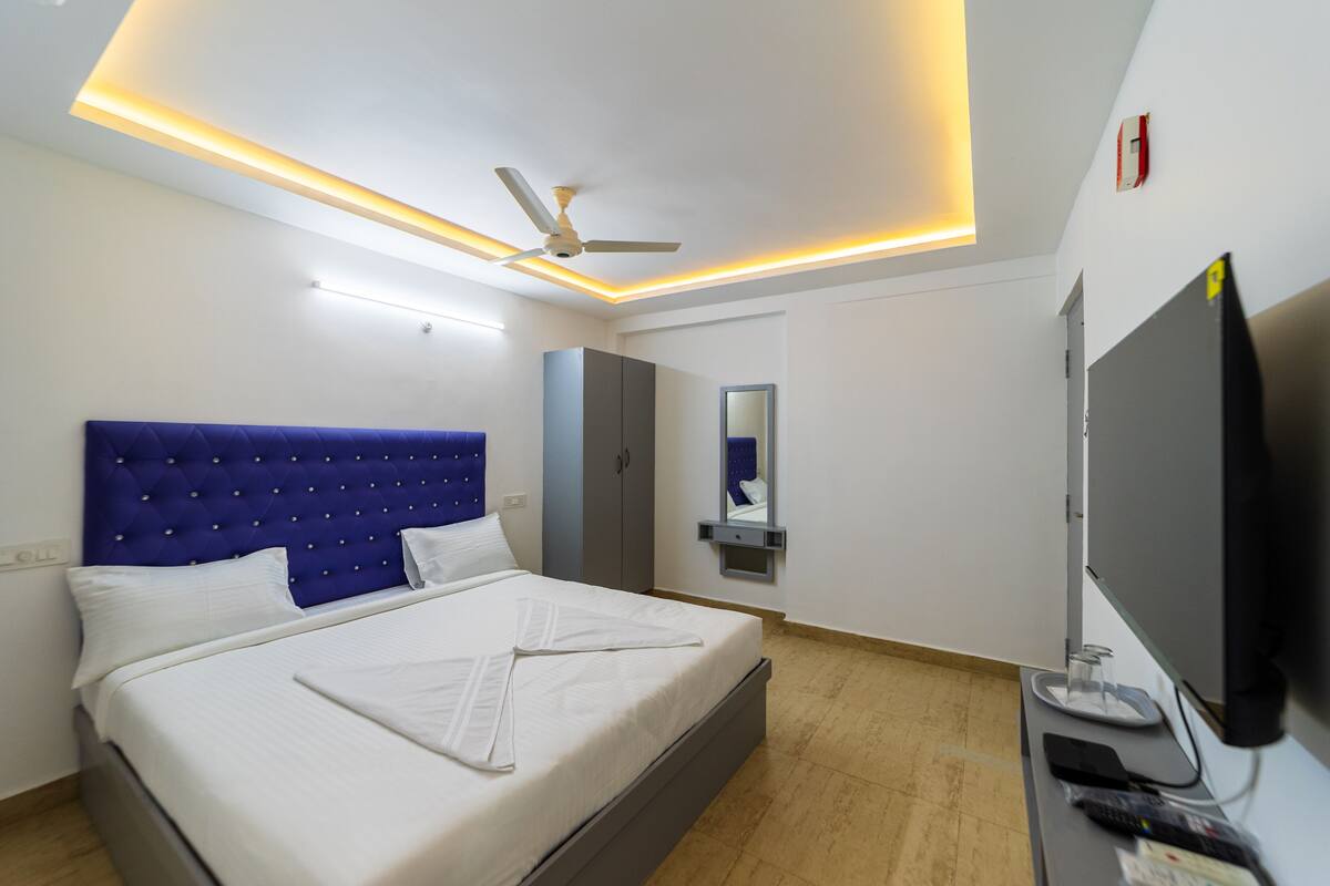 A modern hotel room with a large bed, a ceiling fan, a flat-screen TV, and a bedside table with a remote control.