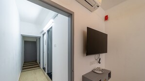 A hallway with a flat-screen TV mounted on the wall, a small console table, and a door at the end.