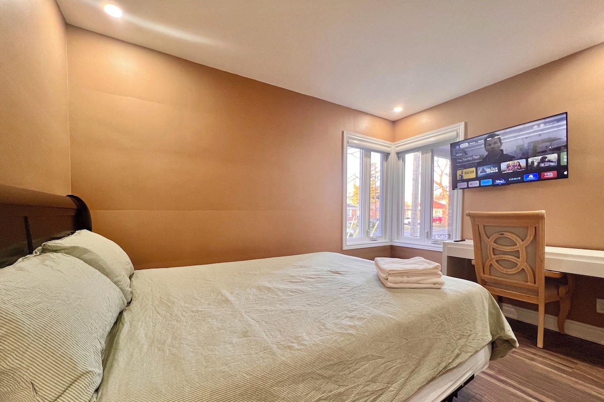 Un dormitorio con una cama, una silla, un escritorio y un televisor montado en la pared.