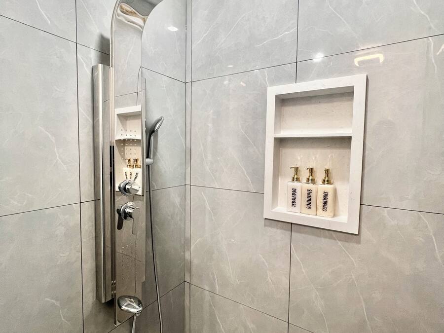 A modern bathroom with a shower, a vanity with a mirror, and a shelf with toiletries.