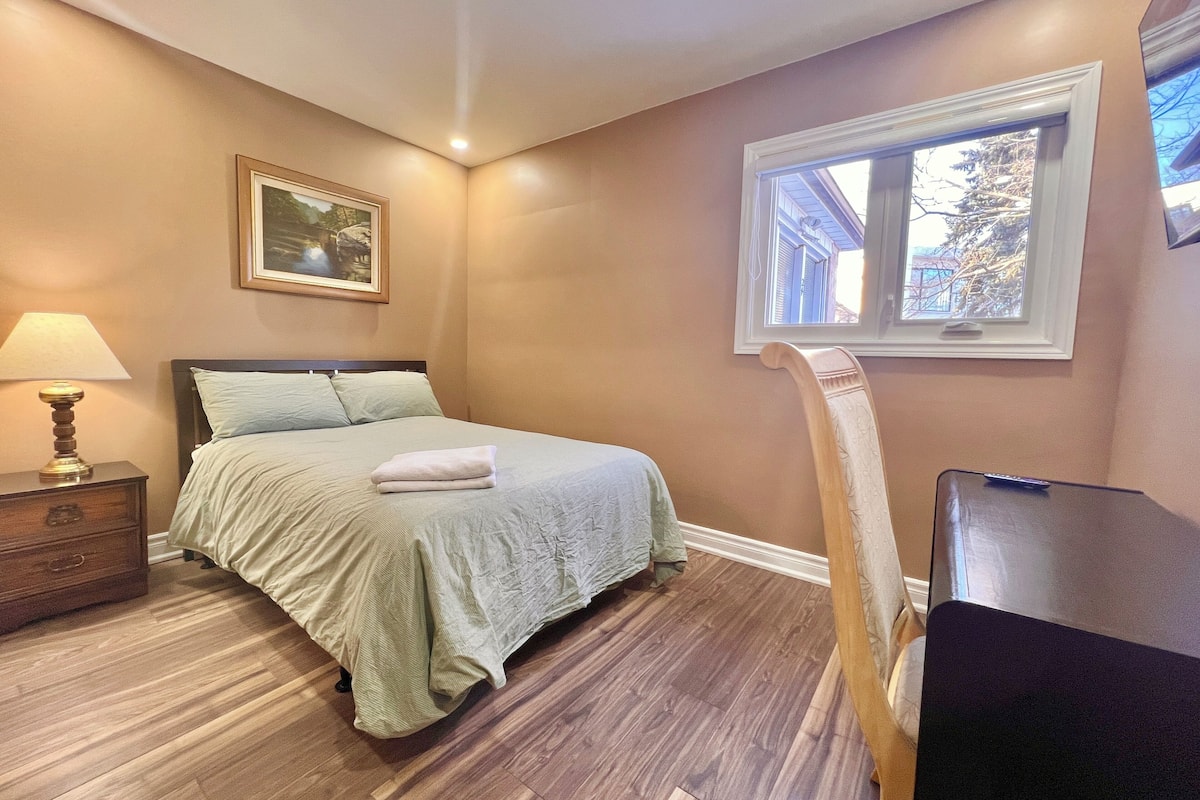 Un dormitorio con cama, mesita de noche, lámpara, ventana y una silla.